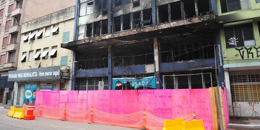 Dois dias após incêndio fatal, tapumes e flores penduradas compõem cenário de pousada em Porto Alegre